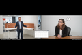 Video call between a GLSC product specialist in the showroom gesturing at an OE1 workstation and a client at their desk, with a product spec sheet visible on screen