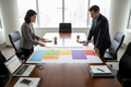 Large printed 8-week move sequence diagram on a conference table with a project manager walking a client through color-coded phases from pre-move audit through occupancy