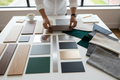 Designer's hands arranging wood veneer, laminate, metal finish, and fabric memo samples into coordinated groupings on a large work surface